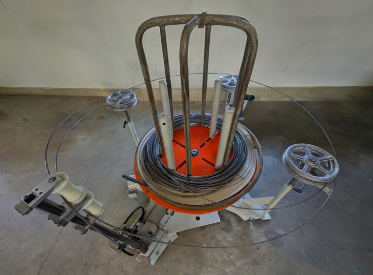 Industrial wire reel with coiled wire and an orange base in a workshop setting